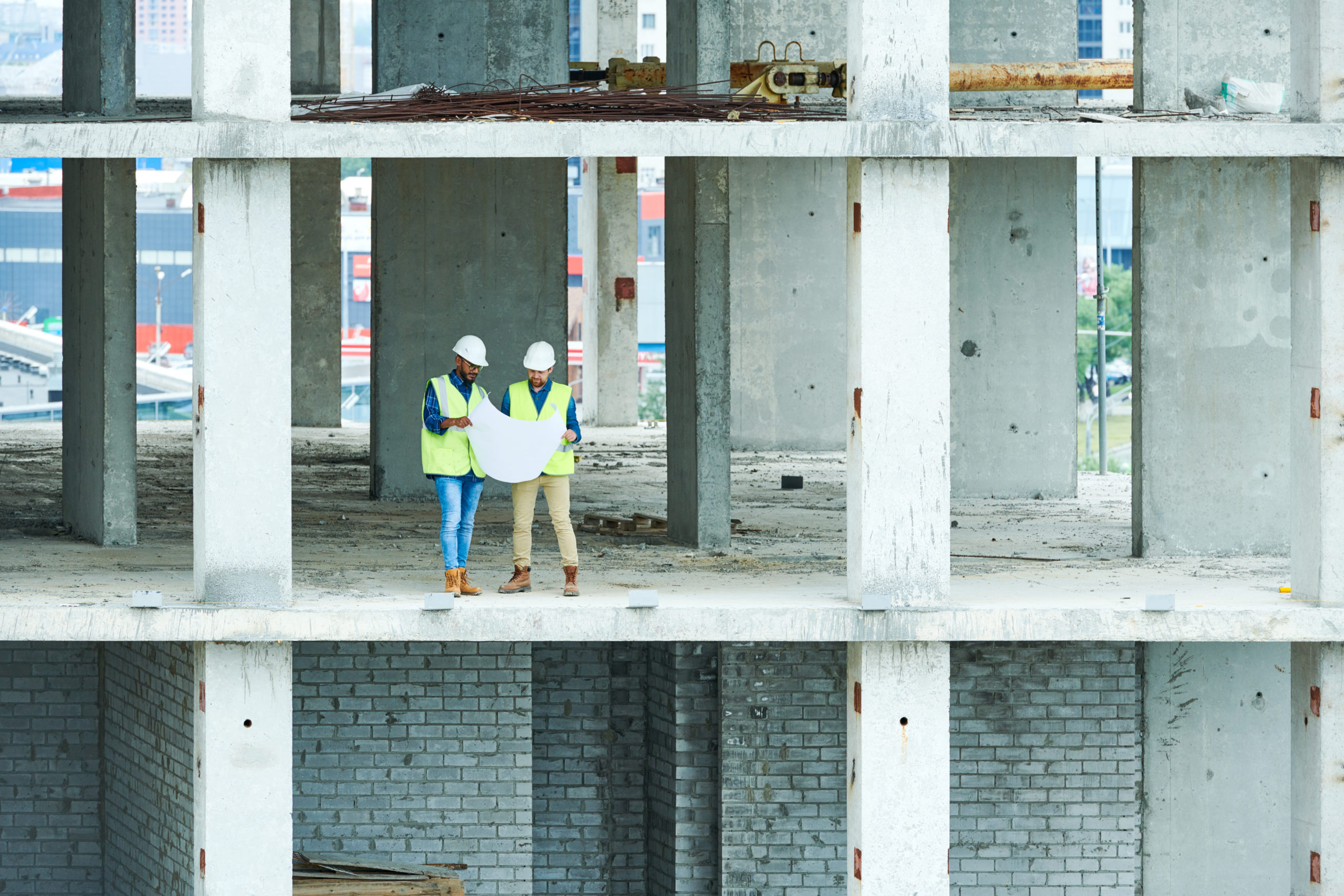 Wide angle view at two builders holding plans standing in unfinished apartment building on construction site, copy space